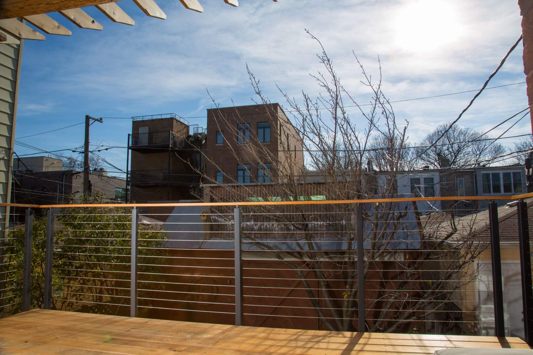 This porch overlooks a residential area. The houses across the street are brick, and there is a tree right in front of the wired railing.