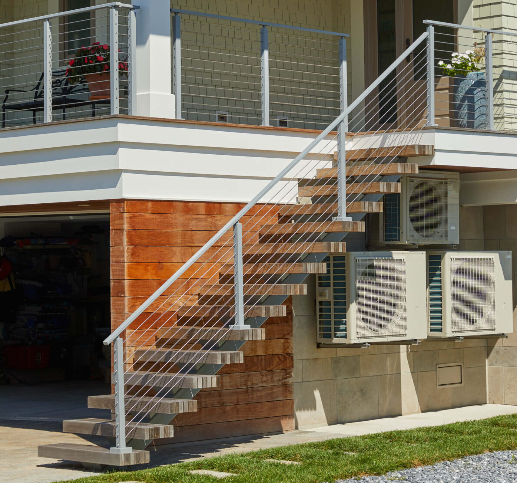 This outdoor staircase leads up to the second-floor terrace. There are three HVAC systems below the steps. The metal railing is a light grey coloring. 